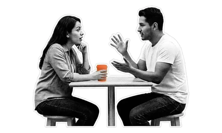 Dos personas conversando frente a frente en una mesa, con una taza naranja