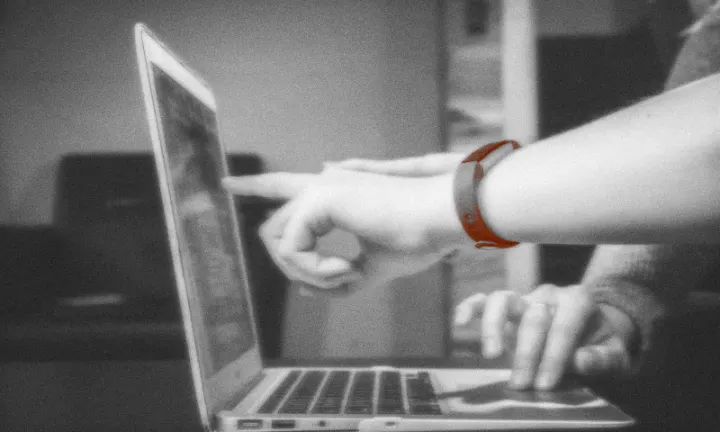 Una mano señala la pantalla de una laptop mientras otra usa el panel táctil