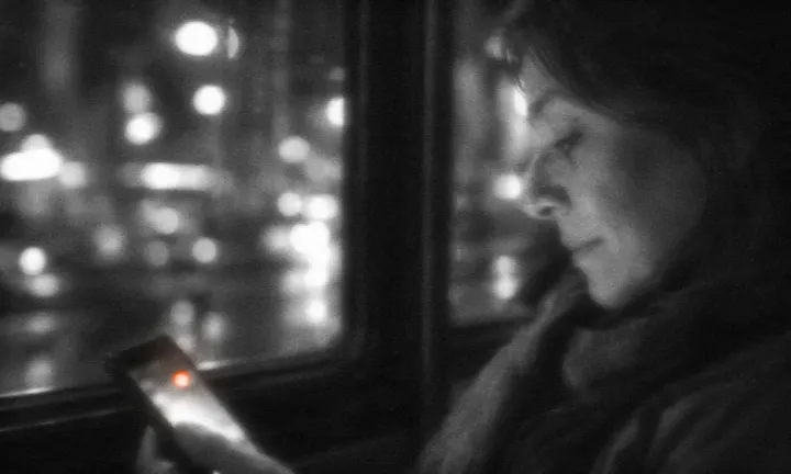 Mujer de perfil en un colectivo de noche que mira la pantalla de su celular, con una notificación y las luces de la ciudad desenfocadas detrás